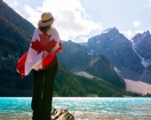 Une personne avec un drapeau canadien sur son dos, regardant le parc national Banff, qui est le plus fréquenté au Canada.   — Photo : @andre-furtado – Pexels