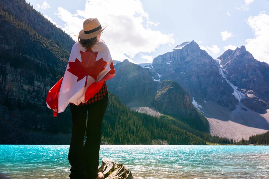 Une personne avec un drapeau canadien sur son dos, regardant le parc national Banff, qui est le plus fréquenté au Canada.   — Photo : @andre-furtado – Pexels