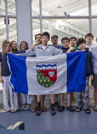 Tony Shi, au centre, tenant le drapeau ténois au côté de ses équipiers et de ses coachs au Centre aquatique de Yellowknife peu de temps avant de s'envoler vers les Jeux d'été du Canada 2025. &mdash; Ollie Williams/Team NT