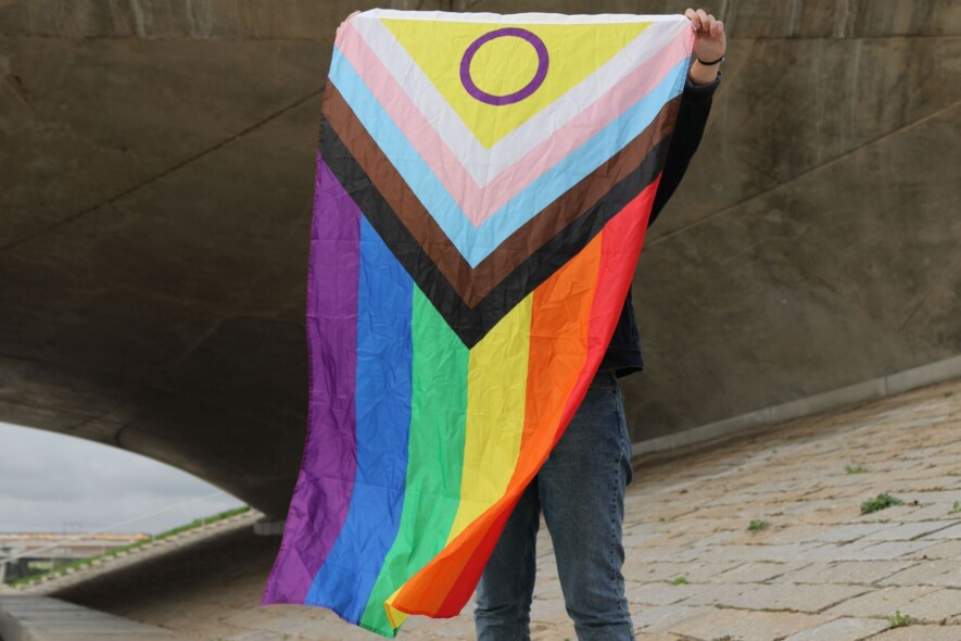  Une personne sous un pont tenant un drapeau de fierté inclusif, symbolisant la diversité.
 &mdash; Crédit : Pexels