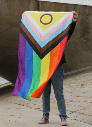  Une personne sous un pont tenant un drapeau de fierté inclusif, symbolisant la diversité.
 &mdash; Crédit : Pexels