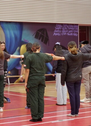 Devant les murs magnifiquement décorés de leur école, les Rangers juniors d’Aupaluk suivent le drill – cette séquence d’exercices dictés par le sergent Martin Scott (tout à droite), et la sergente Amelia Grey (de face, au centre).                                                                                        &mdash; Crédit : François Bellemare 