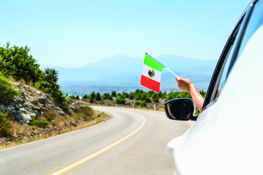 Woman holding Mexico flag from the open car window driving along the serpentine road in the mountains. Concept  