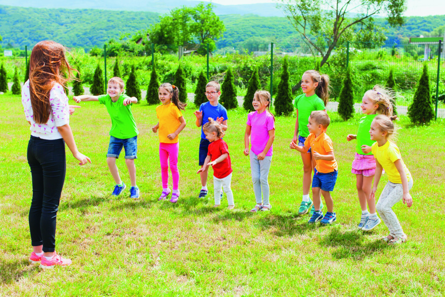 Children with teacher have fun outdoor on the green lawn in the summer camp  