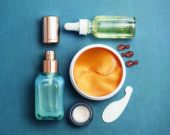 Face serum bottle with face creams, face oil capsules and eye patches on teal blue background. cosmetics flat lay.  