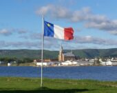 Le drapeau acadien flotte dans une brise estivale chaude avec le village de Chéticamp en arrière-plan ainsi que le magnifique édifice historique, l’Église Saint-Pierre. &mdash; Rosie AuCoin-Grace