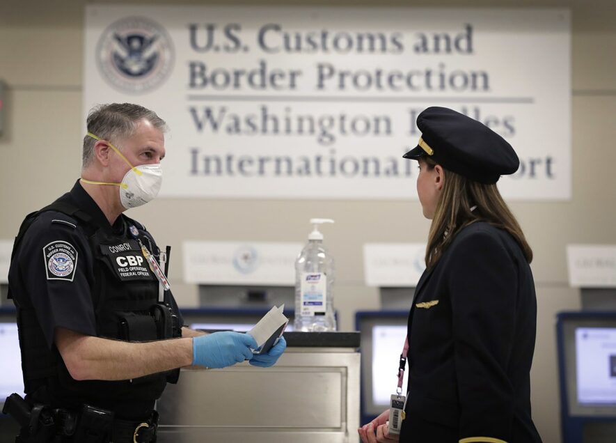 Aéroport international de Washington-Dulles, 18 mars 2020 : un agent du Service des douanes et de la protection des frontières des États-Unis accueille une pilote d’une ligne aérienne internationale — Glenn Fawcett ; source : https://www.flickr.com/photos/cbpphotos/49679050593/, image dans le domaine public.