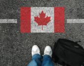 Une personne avec des chaussures et un sac à dos, qui se tient à côté du drapeau du Canada.
 &mdash; PHOTO : Mirsad - Adobe Stock